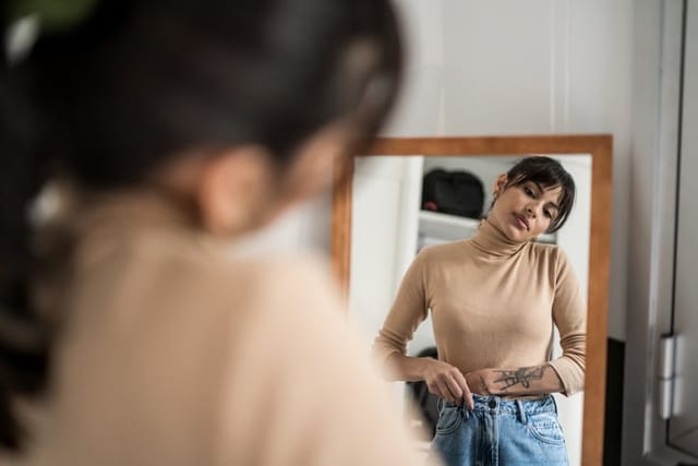 woman examining her body in mirror