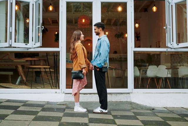 Smiling young couple holding hands together and standing face to face on a sidewalk outside of a cafe