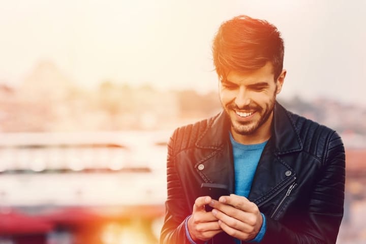 smiling guy texting outside sunset
