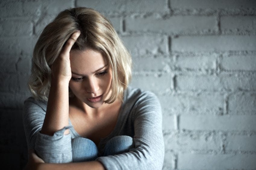 Blonde woman sitting down while looking severely depressed