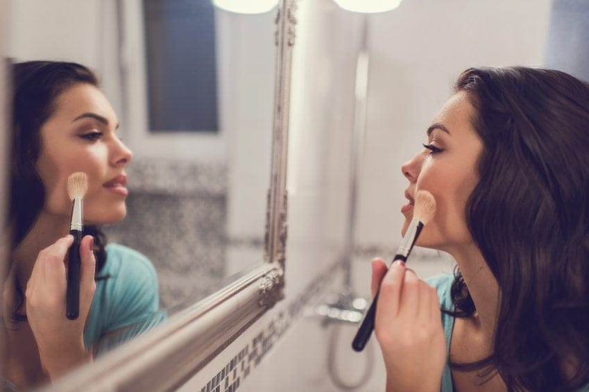 Young woman applying face powder in bathroom