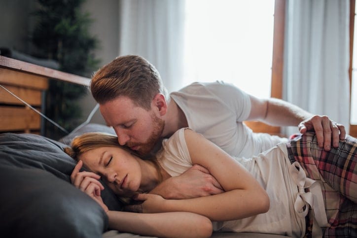 man kissing sleeping woman's cheek