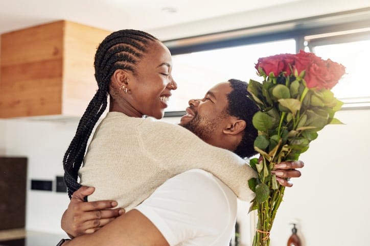 Young man surprising his wife with a bunch of flowers.