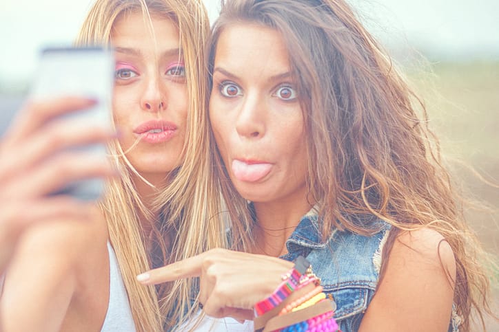 Two cheerful hipster friends taking selfie photos on smart phone
