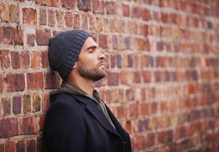 Man leaning against a brick wall in an urban setting.