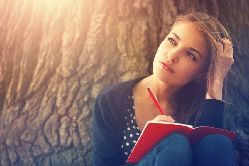 Girl sitting by tree writing journal