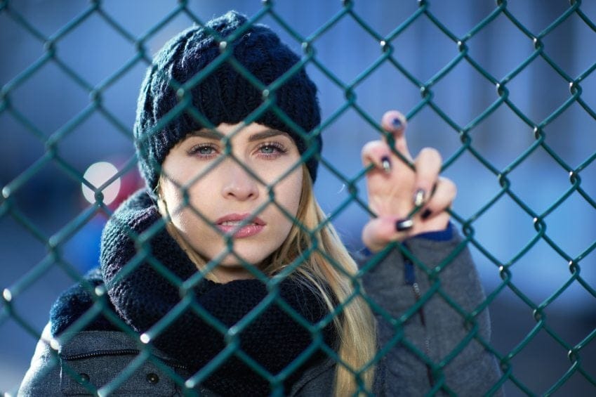 Blonde in hat behind fence