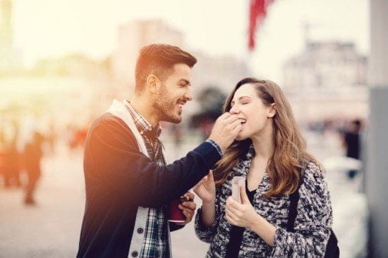 man feeding woman snacks on street