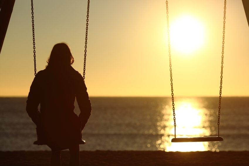 sad woman alone on swing at sunset