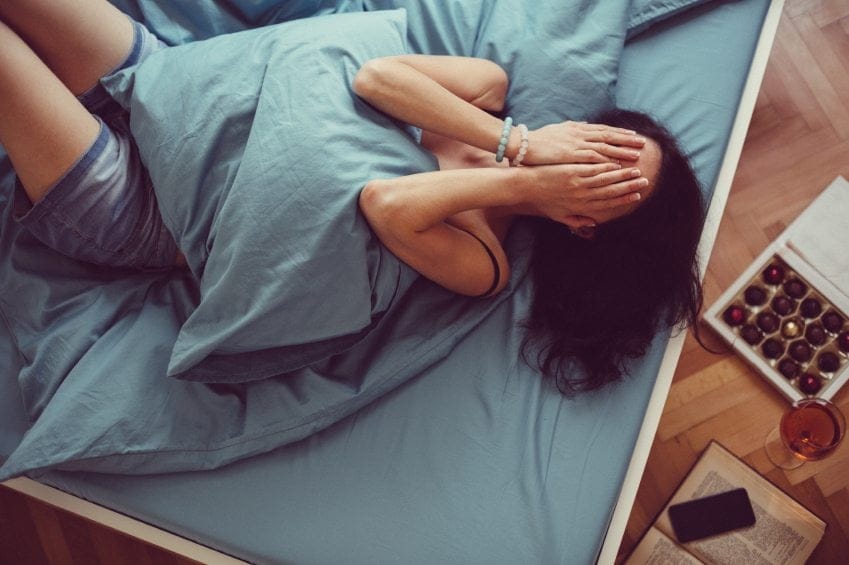depressed woman covering face with hands in bed