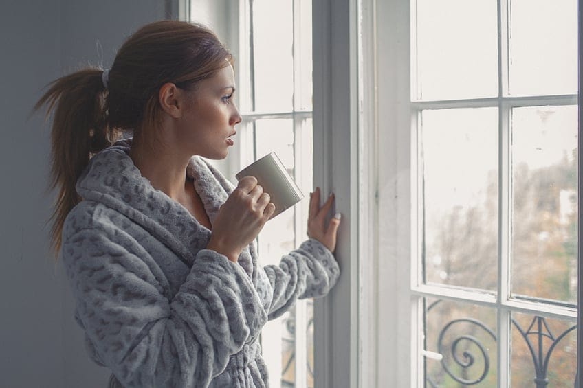 Young woman drinks morning coffee, looking through the window