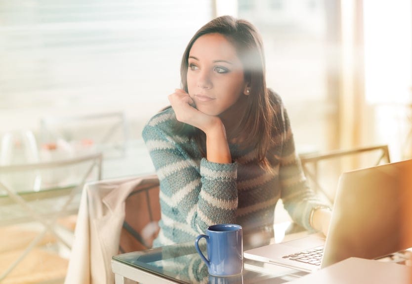 Pensive woman with hand on chin working with her laptop