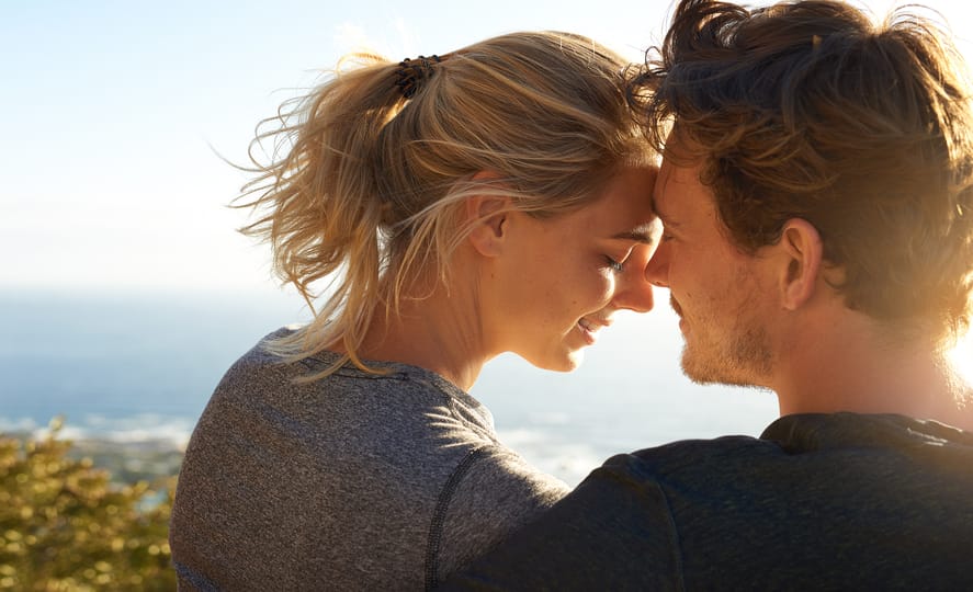 Shot of a loving couple sitting on a bench overlooking the ocean