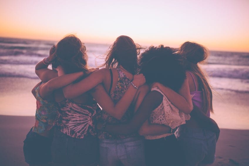 Girl friends hugging and watching the ocean after sunset
