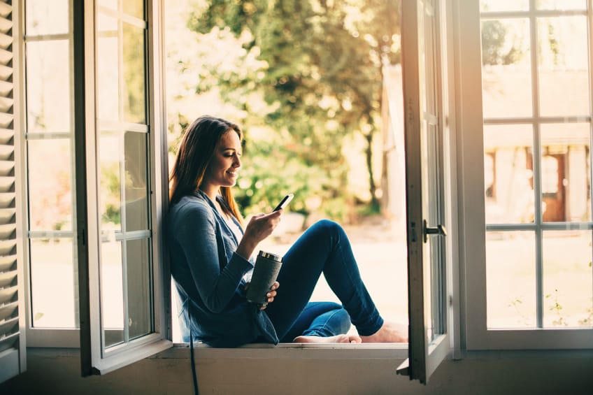 Beautiful young woman holding a cup of coffee an texting at home