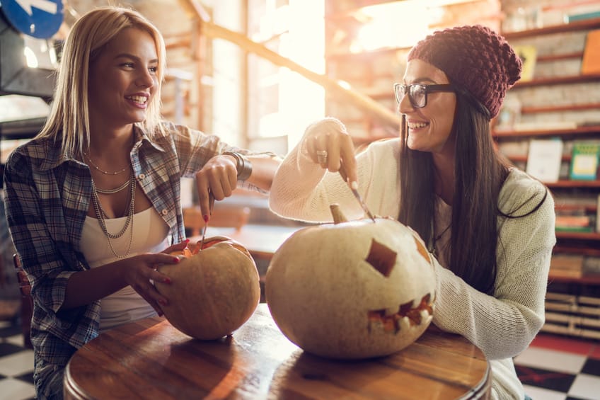 Smiling friends communicating while carving pumpkins for Halloween.