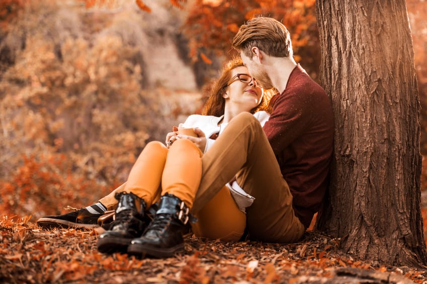 Happy red-haired couple sitting embraced in the park and enjoying in autumn day.