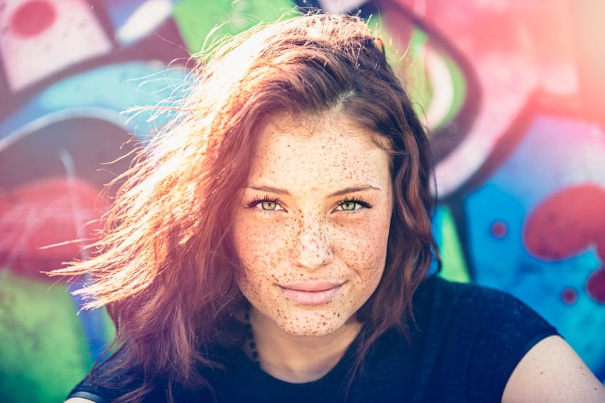 Woman with freckles smiling outside.