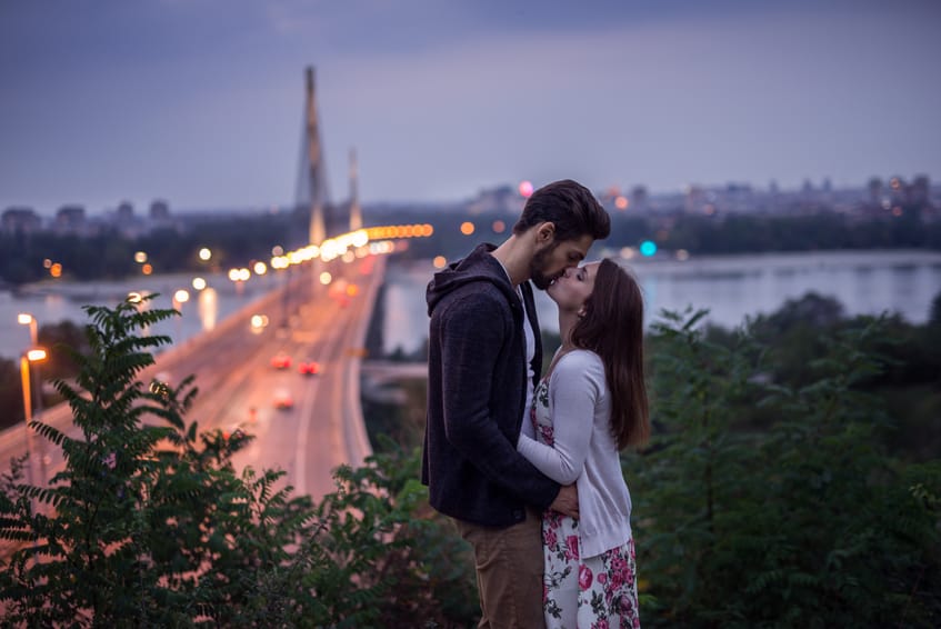 Young couple kissing each other in front of the city lights. High ISO, grainy image.