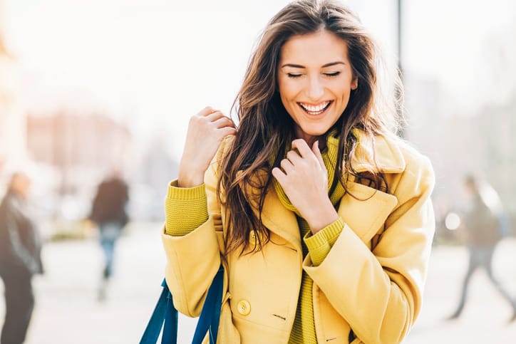 Beautiful young woman smiling and walking outdoors in the city, with sunlight and copy space