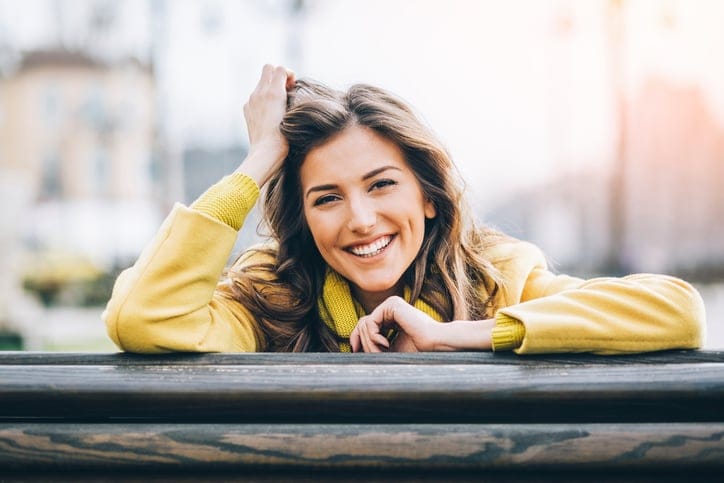 Beautiful smiling woman sitting on a bench enjoying the sunlight outdoors in the city, with copy space