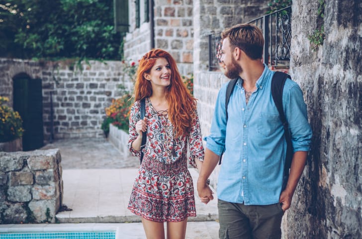 Young tourist couple, walking through the old city. Holding hands. Wearing casual clothes and backpacks. Enjoying in beautiful exploring day.