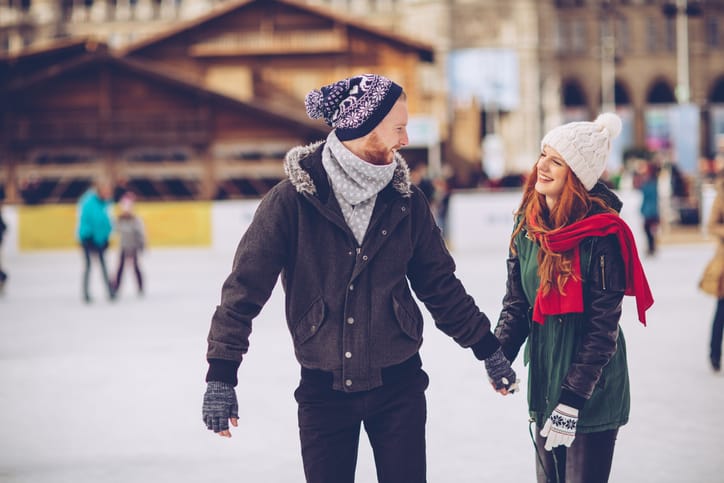 Romantic coupleholding hands on the ice rink in the winter. The couple is wearing casual winter coats and ice skates, standing on the ice together.