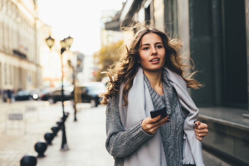 A young woman texting on the phone and rushing down the street.