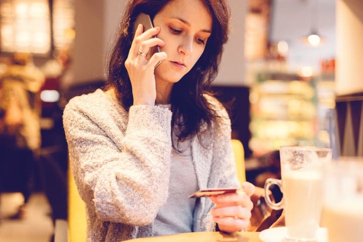 Young woman in a cafe phoning the bank for credit card support.
