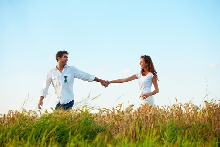 A couple holding hands while walking through a wheat field on a sunny day