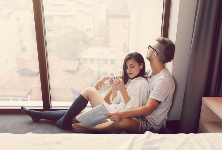 Beautiful young heterosexual couple sitting by the window embraced, enjoying their carefree weekend morning together.
