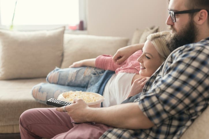 couple watching movies on the couch eating popcorn.