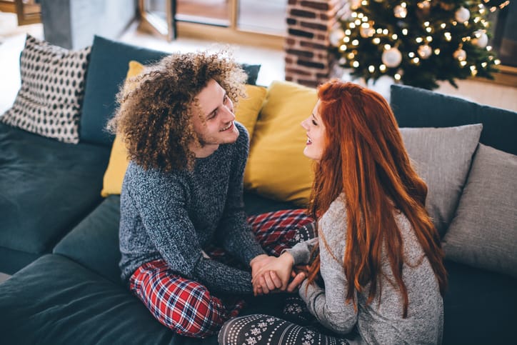 Happy young couple sitting on sofa and embracing. Wearing pajamas. Christmas tree in background. Having fun.