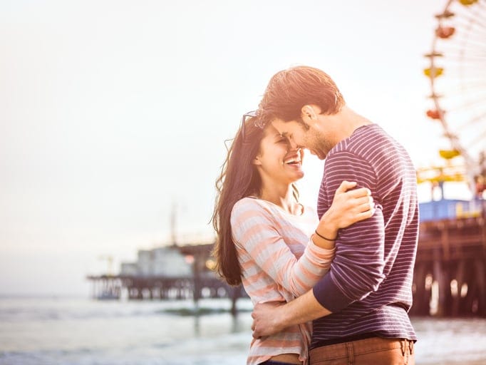 Happy couple on LA beach next to amusement park.