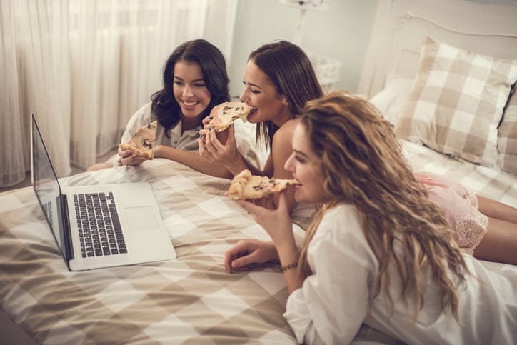 Three women relaxing on a bed together using computer.