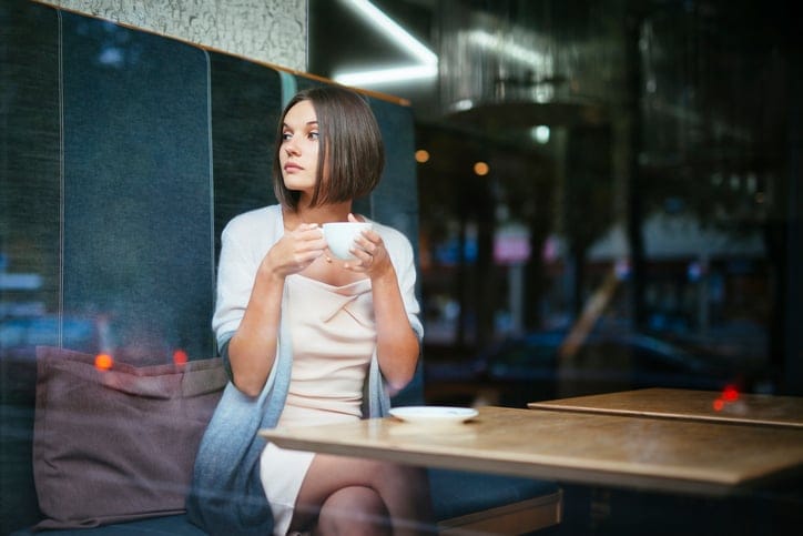 Girl inside the cafeteria sitting by the window glass with cup of tea