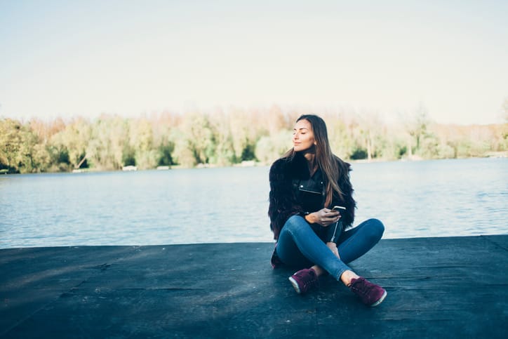 Young woman sitting on jetty and using smart phone