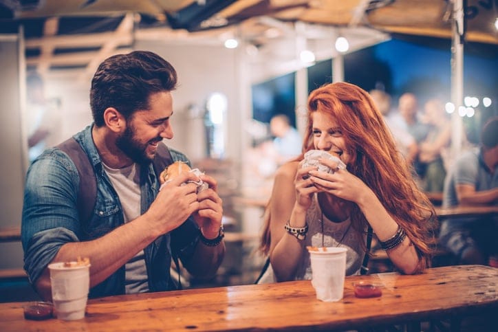 A young couple having snack and drink at an outdoors music festival. Eating burgers with fries and drinking beer.