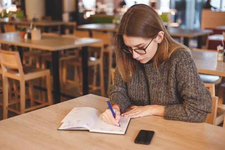 young woman writing journal office