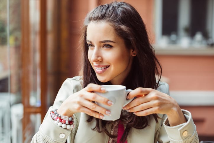 Smiling woman drinking coffee and looking through the window