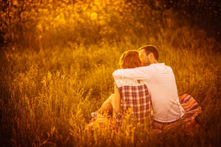 Photo of young couple sitting and hugging in a meadow