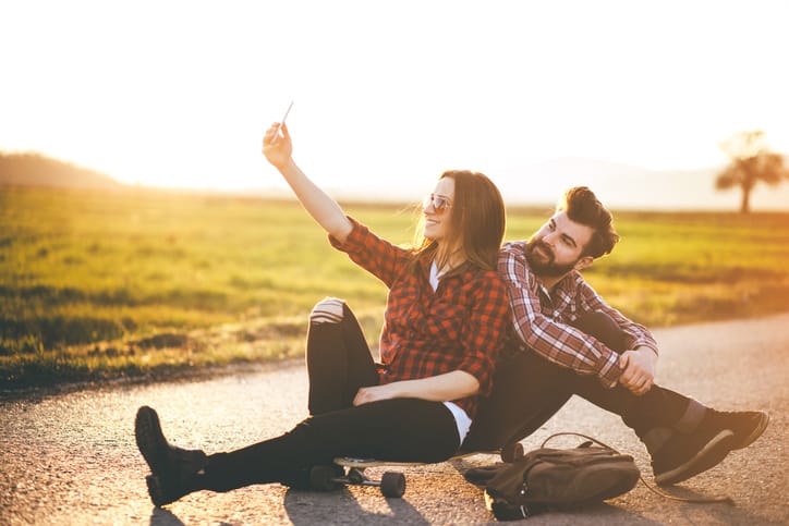 Cute couple of skaters sitting on the longboard and taking selfies with smart phone