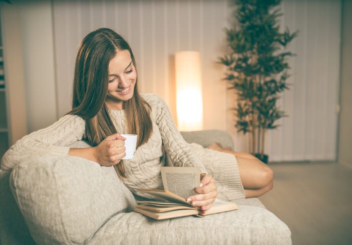 Young brunette reading book and drinking coffee on sofa
