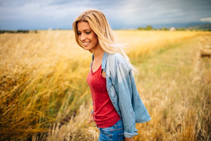 Photo of a young woman standing in the middle of a wheat field, feeling free and happy