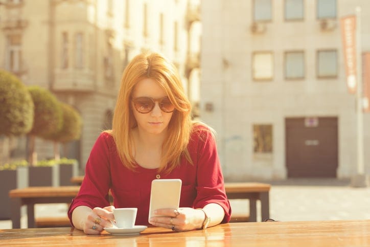 Stylish woman drinking coffee and using her cellphone outdoors.