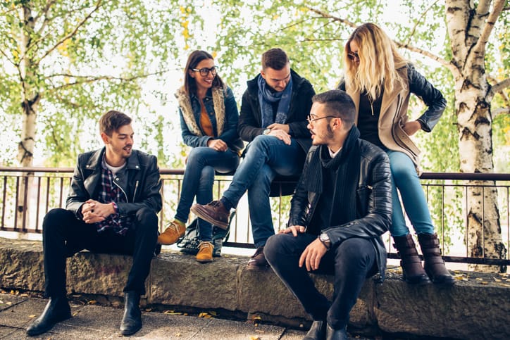 Group of friends sitting outdoors, talking to eachother, having fun and enjoying the sunny day.