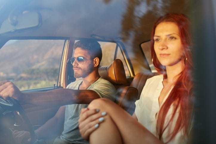 Outdoors shot of a young couple on road trip. Man driving are on summer day with his girlfriend.