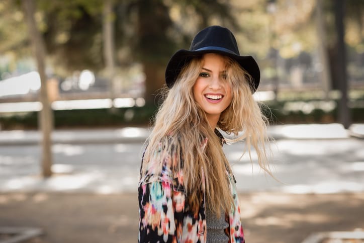 Portrait of beautiful young woman looking at camera playing with her curly hair and smiling. Girl wearing jacket and hat.