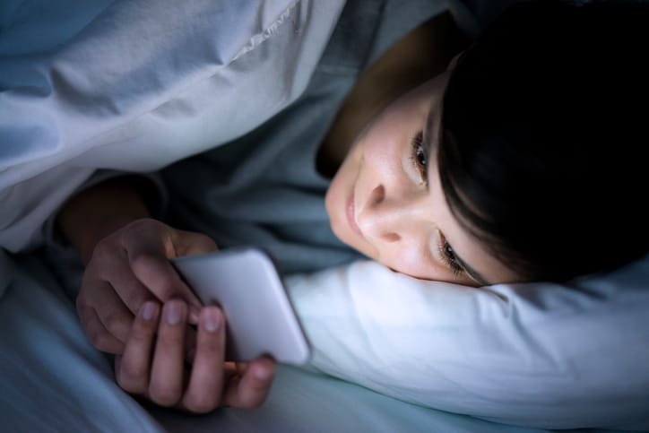 young woman phone bed dark