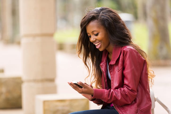 cheerful african woman using smart phone outdoors